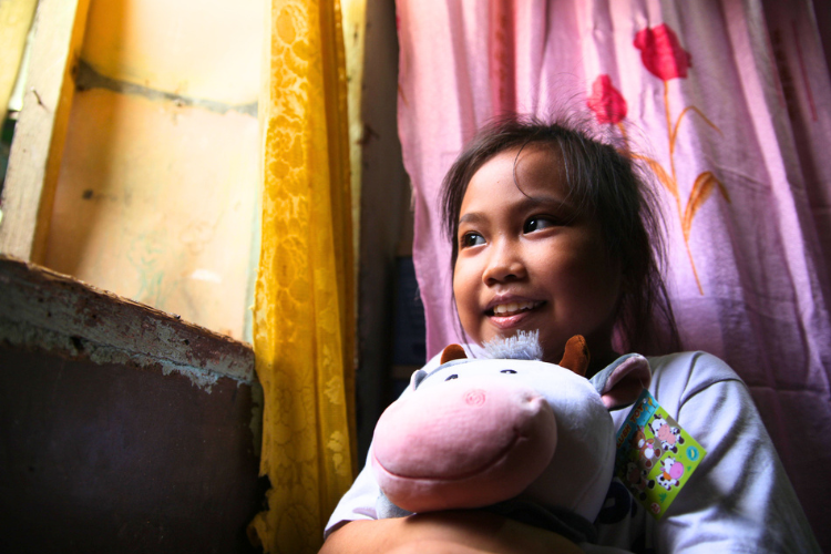 a smiling little girl holds a stuffed pig and looks out a widow