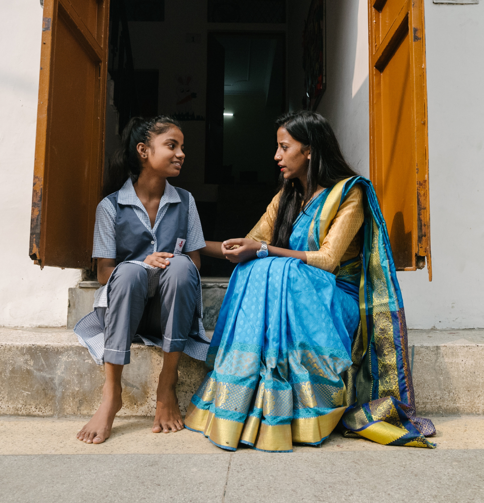 Indian woman sits outside open door on a step next to a girl