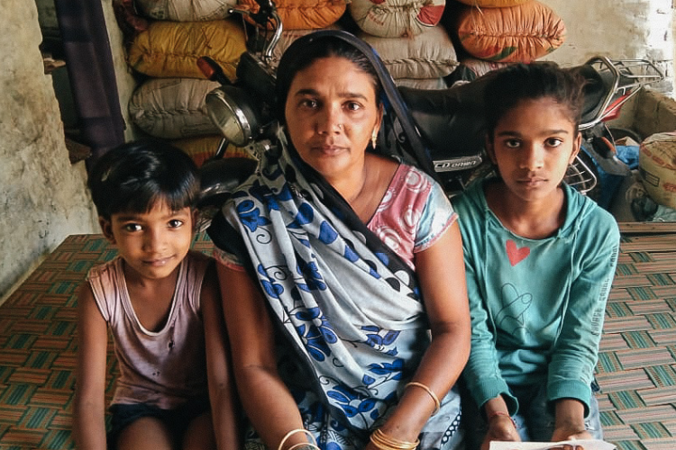 An Indian mother kneel-sitting on a mat with her two children on either side of her