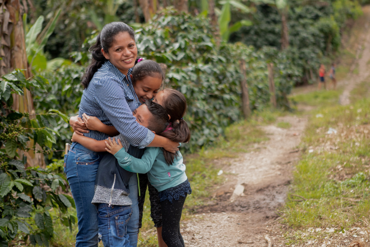 Mother hugging three children outside with a pathway behind them